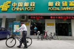 A man pushes his bicycle past a branch of China’s Postal Savings Bank. The lender’s recent announcement is seen by analysts as a bid to improve its corporate governance.