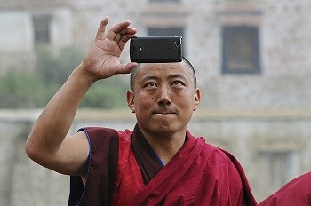 A Tibetan monk takes a picture of himself, a "selfie," using his mobile phone.