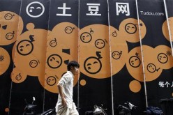 An employee walks past the logo of Youku Tudou at the company's headquarters in Beijing, China.