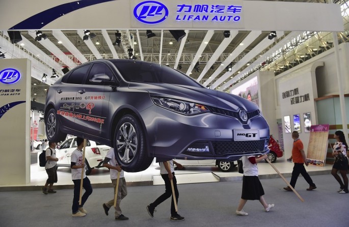 Employees carry an ad for an SAIC Motor car during the Wuhan 2014 Motor Show. 