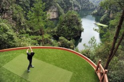 A golf player hits a shot toward a putting green on a lake from a tee ground on top of a hill, at Zhangjiajie, Hunan Province, Sept. 23, 2014.