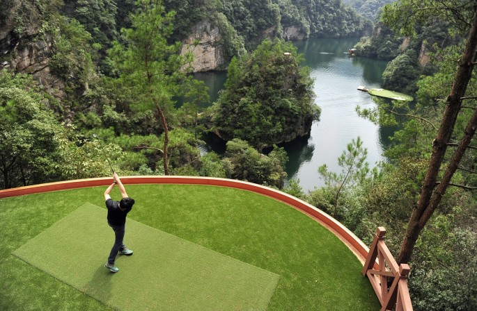 A staff member plays a shot toward a putting green on a lake from a tee ground on top of a hill, at Zhangjiajie, Hunan Province. 