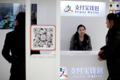 A sales assistant sits behind and under Alipay logos at a train station in Shanghai. ShopRunner hopes to increase its presence in China using its partnerships with Alibaba and Alipay.