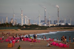Windmills and a power plant can be seen in the distance as beachgoers watch sunset in the city of Dongfang on the western side of China's island province of Hainan.