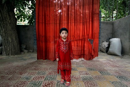 An ethnic Uyghur girl poses for photo in front of a red curtain at her home in Hetian, Xinjiang Uyghur Autonomous Region.