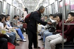 An elderly beggar tries to solicit money from subway passengers on a Beijing subway train. 