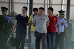 The suspected leader of a gang that allegedly hired university students to impersonate test takers for the gaokao is escorted by officers in a train station in Heze City, Shandong Province, on June 8.