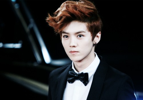 Lu Han, wearing an earring, poses for the camera in a suit and bowtie.
