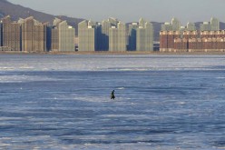 A fisherman walks on the partially frozen Jinzhou Bay of the Bohai Sea near residential construction sites in Dalian, Liaoning Province, in this Dec. 17, 2014 photo.