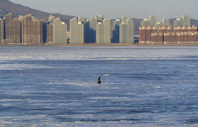 A fisherman walks on the partially frozen Jinzhou Bay of the Bohai Sea near residential construction sites in Dalian, Liaoning Province, in this Dec. 17, 2014 photo.
