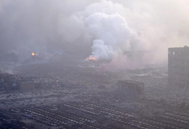 Smoke rises from the debris near damaged vehicles after the explosions at the Binhai new district in Tianjin, China, Aug. 13, 2015.