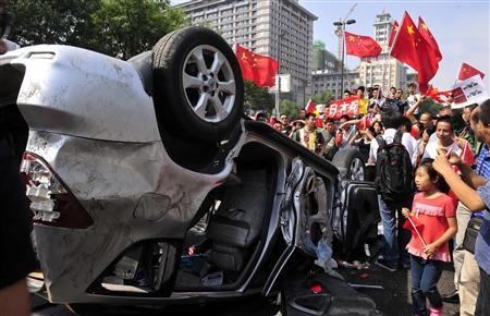 Demonstrators hold Chinese flags and banners beside an overturned car of a Japanese brand during a protest in Xi'an, Shaanxi Province, in this Sept. 15, 2012 file photo.