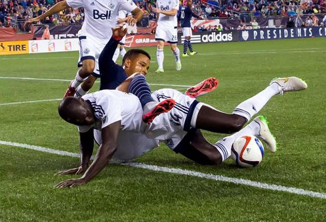 Vancouver Whitecaps defender Pa Modou Kah (#44) takes down New England Revolution forward Charlie Davies in an MLS soccer match.