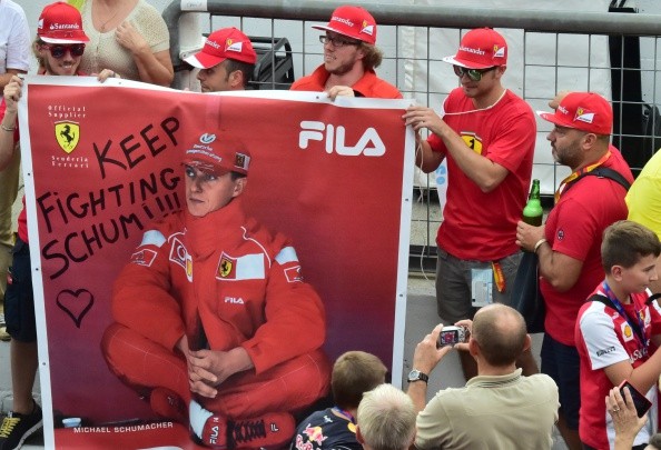 A man takes a photograph of Scuderia Ferrari's supporters as they hold a banner with Michael Schumacher's photo on it. 