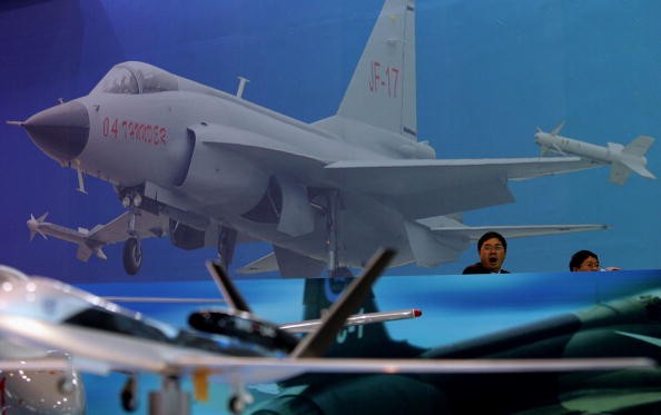 Visitors sit in front of an illustration of a Chinese-made JF-17 fighter jet at Airshow China 2006 in Zhuhai, south China's Guangdong Province, on Nov. 1, 2006.