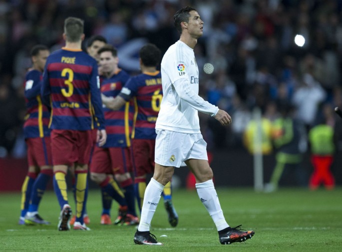 Real Madrid forward Cristiano Ronaldo (R) walks off the pitch as Lionel  Messi and the rest of his Barcelona teammates celebrate in the background.