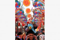 A child with a pinwheel enjoys a shoulder ride at the temple fair in Ditan Park in Beijing, capital of China, Feb. 8, 2016.