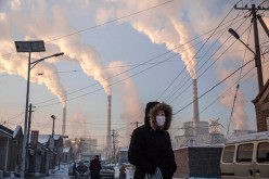 Smoke billows from stacks as a Chinese woman wears as mask while walking in a neighborhood next to a coal fired power plant on Nov. 26, 2015 in Shanxi, China.