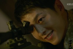 Captain Yoo Shi Jin, played by Song Joong-ki, is using his rifle scope to spy on Dr. Mo Yeon (Song Hye-Kyo) while washing her face outside the base camp.