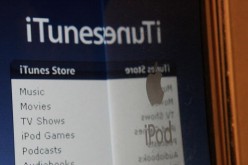 An Apple iPod is held near the iTunes website displayed on a computer screen.  