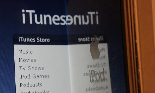 An Apple iPod is held near the iTunes website displayed on a computer screen.  